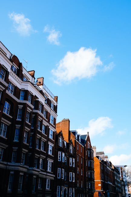The image depicts a row of Georgian-style terraced houses with red brick facades accented by decorative white trim around the tall, arched windows and doorways. Each property features black wrought-ir