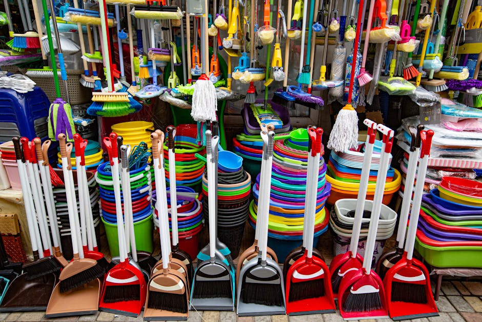 A display of various cleaning tools, including brooms, dustpans, and mops with colorful plastic buckets and stacking trays arranged on a retail store shelf. The surfaces of the tools and containers are clean and shiny, with some of the mop heads and dustcloths hanging neatly. The lighting highlights the vibrant colors of the cleaning equipment, illustrating a well-organized and hygienic cleaning supply area, as seen in a setting that could be part of a commercial or domestic cleaning environment. Including the name Cleaner Putney, this image emphasizes the importance of thorough surface cleaning and maintenance for retail or shop environments on Upper Richmond Road, aligning with professional cleaning standards for hygiene and presentation.