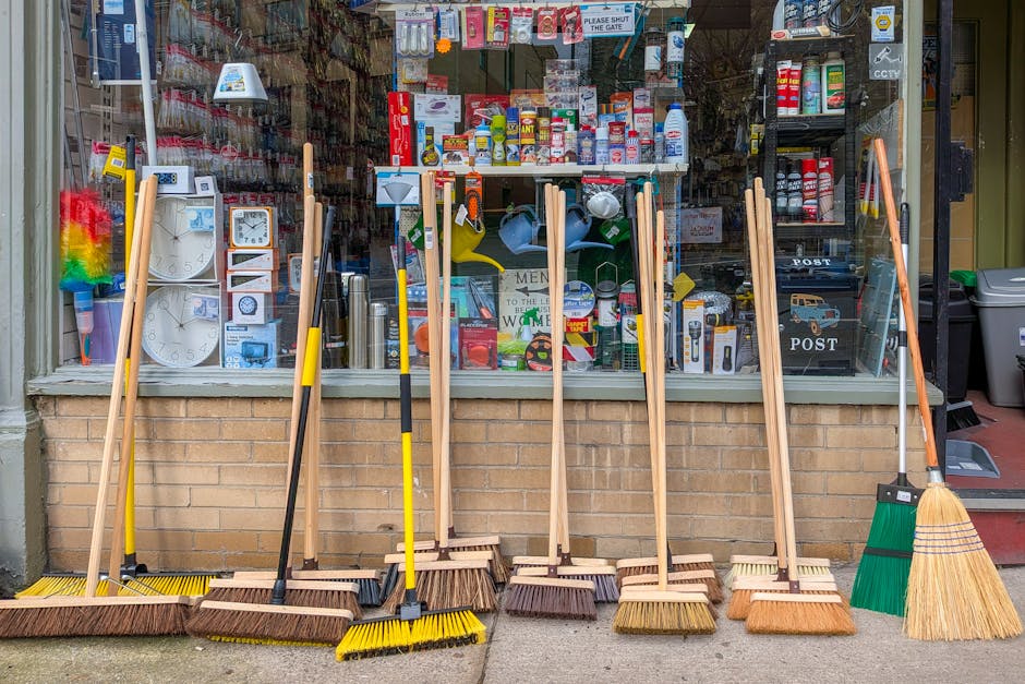 A display of various cleaning tools, including brooms, dustpans, and mops with colorful plastic buckets and stacking trays arranged on a retail store shelf. The surfaces of the tools and containers are clean and shiny, with some of the mop heads and dustcloths hanging neatly. The lighting highlights the vibrant colors of the cleaning equipment, illustrating a well-organized and hygienic cleaning supply area, as seen in a setting that could be part of a commercial or domestic cleaning environment. Including the name Cleaner Putney, this image emphasizes the importance of thorough surface cleaning and maintenance for retail or shop environments on Upper Richmond Road, aligning with professional cleaning standards for hygiene and presentation.